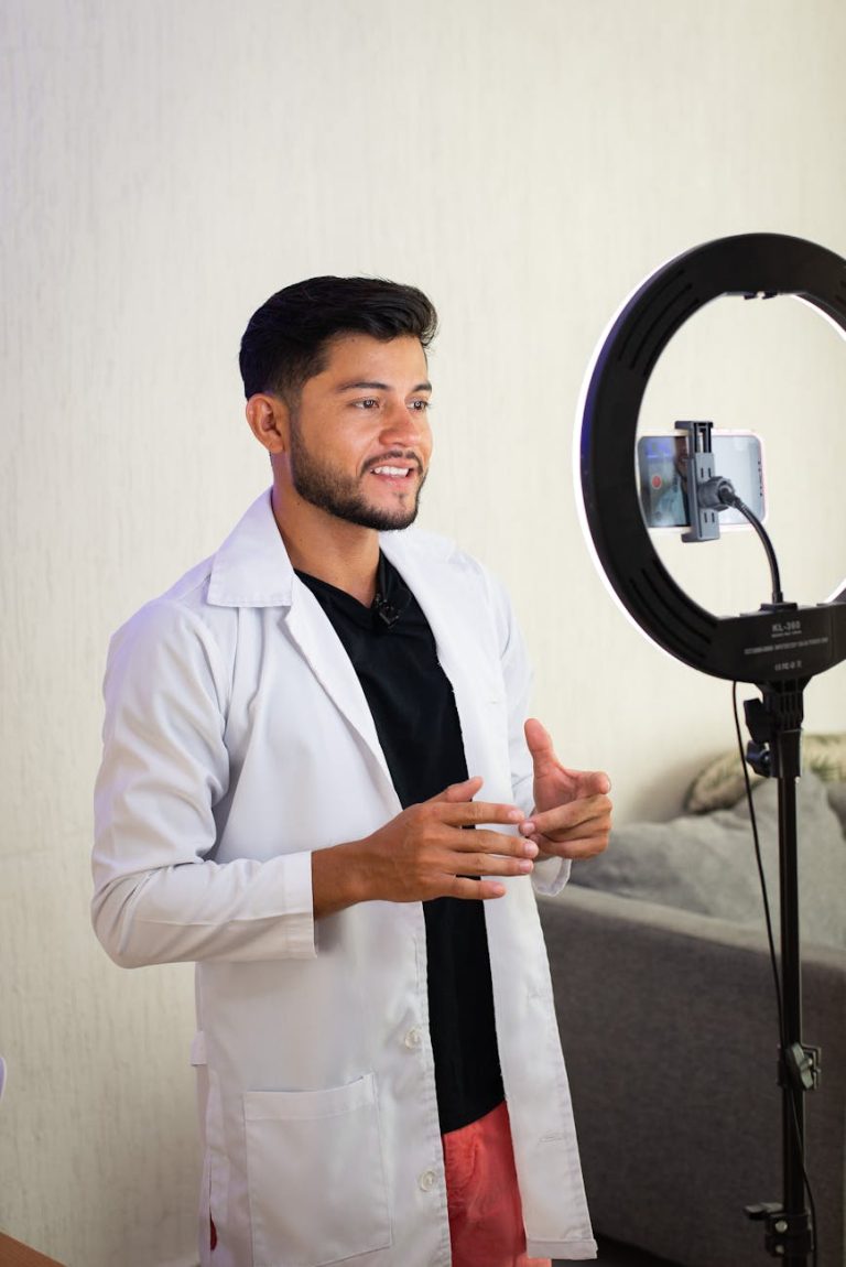 Male doctor in a white coat recording video with a ring light, engaging with the audience.