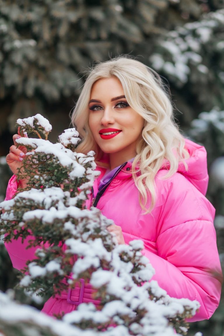 A cheerful young woman in a pink coat explores a snowy forest, capturing the joy of winter outdoors.