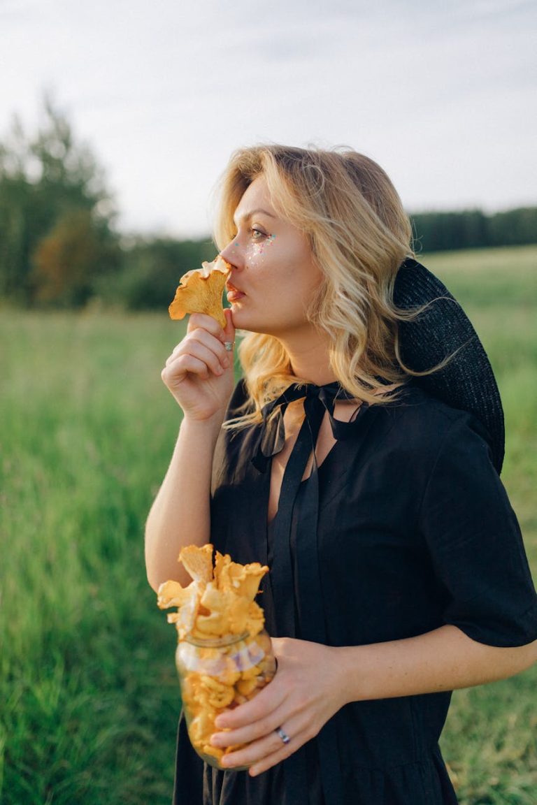 A woman in a black dress enjoys fresh chanterelle mushrooms in a sunny field.