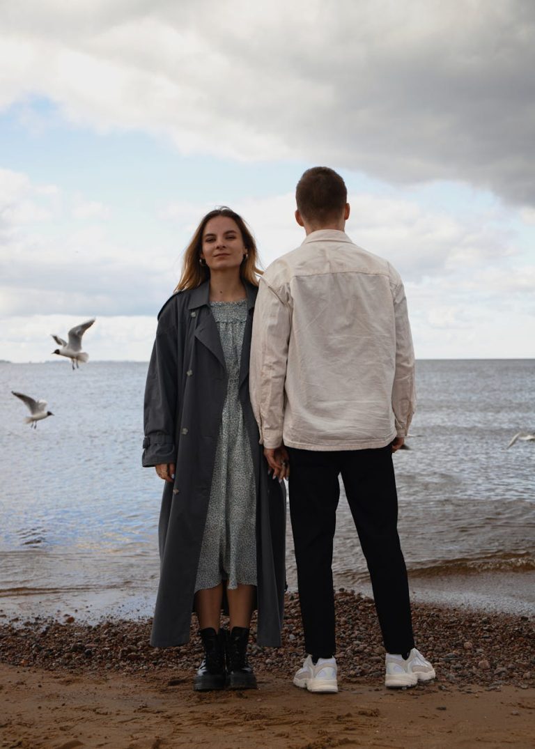 A stylish couple holding hands on a beach in Saint Petersburg with seagulls flying by.