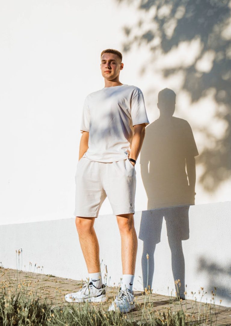 Young man in casual attire stands against a wall, casting a shadow in the summer sun.