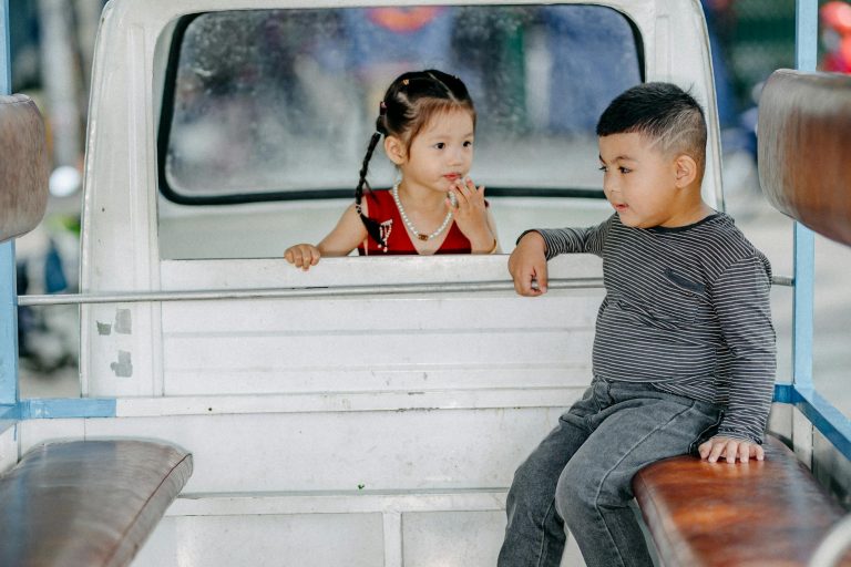 Two young children enjoy a playful moment in the back of a small truck. Urban setting fun.
