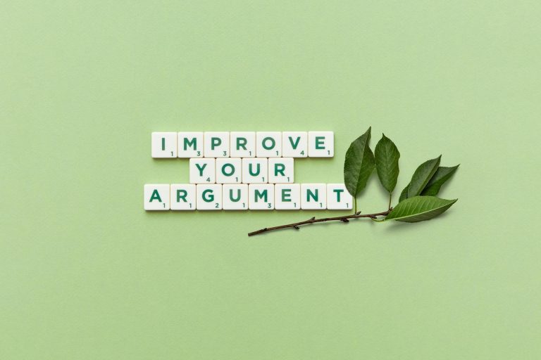 Scrabble tiles spelling 'Improve Your Argument' on a green background with leaves.