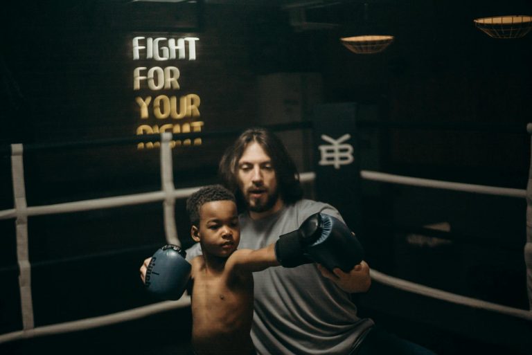 A child practices boxing under the guidance of a coach in an indoor gym setting.