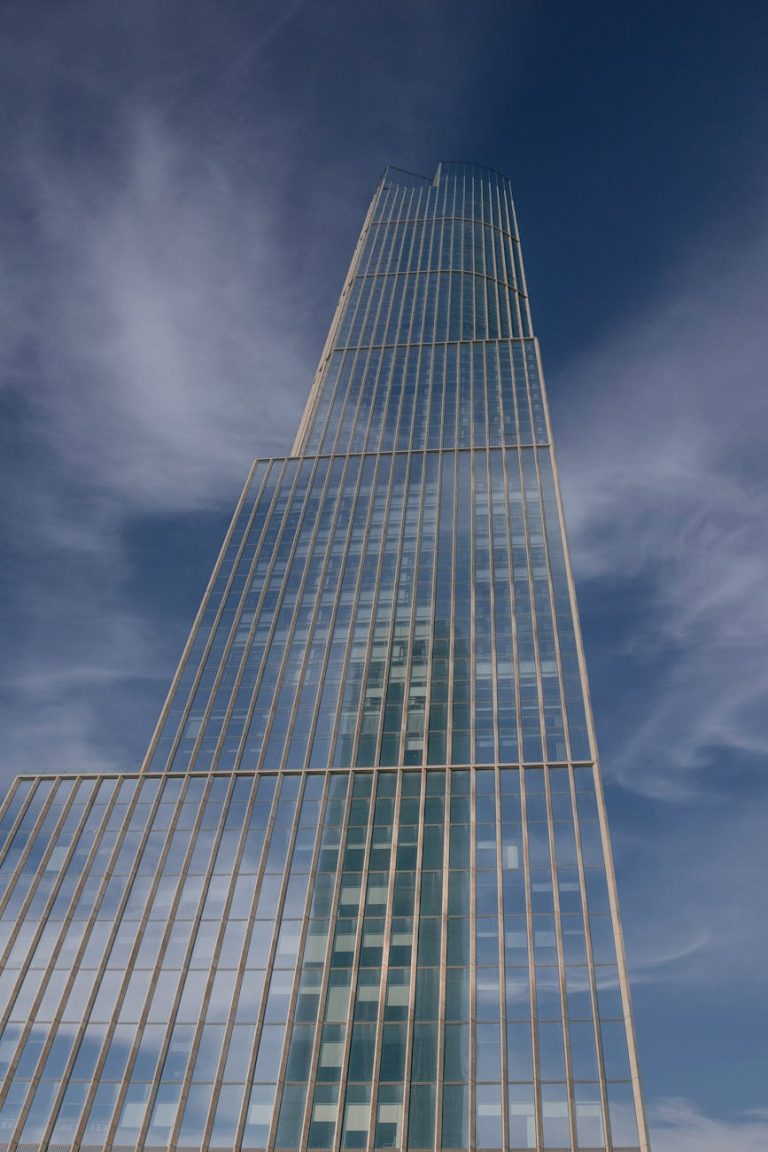 Stunning upward view of a modern skyscraper with a reflective glass facade against a clear blue sky.