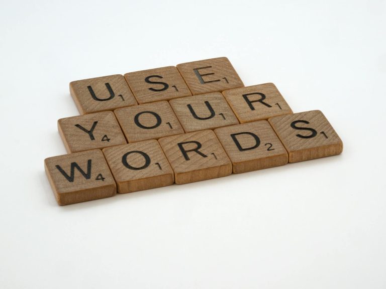 Wooden letter tiles spell 'USE YOUR WORDS' on a white background, promoting linguistic creativity.