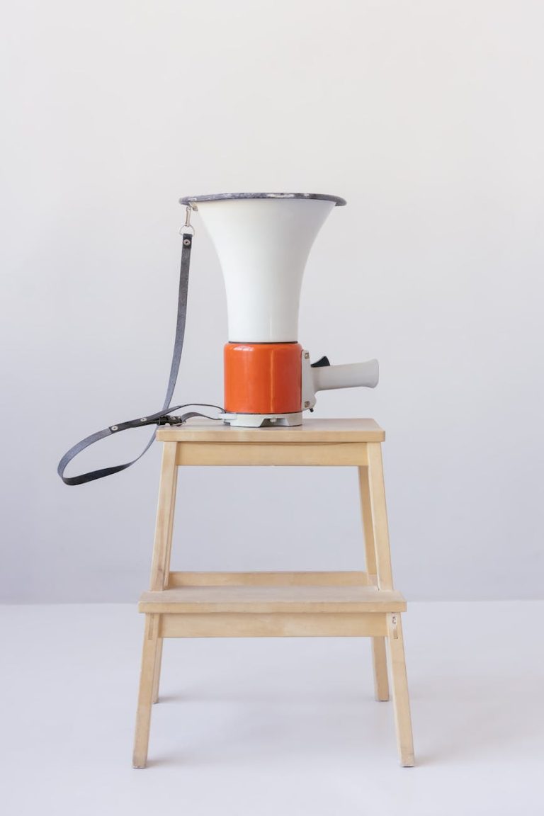A red and white megaphone placed on a wooden stool against a minimalist background.