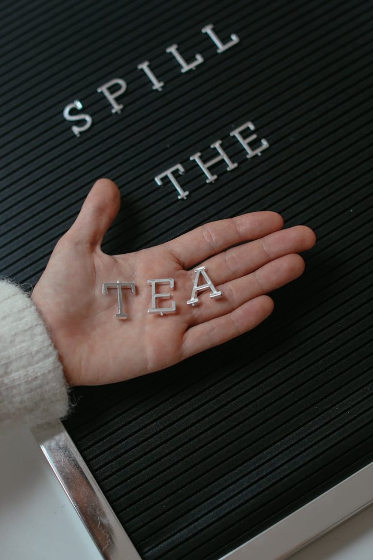 Hand holding letters on a board with the message "Spill the Tea" for trendy expression.